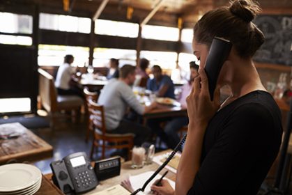 Young woman taking a reservation by phone at a restaurant Young woman taking a reservation by phone at a restaurant